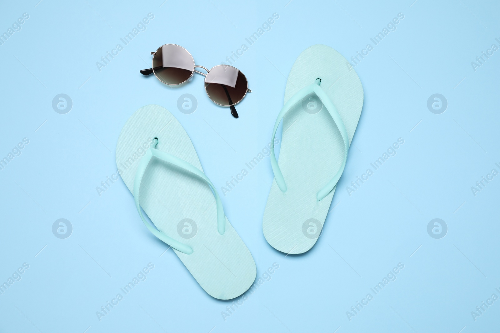 Photo of Flip flops and sunglasses on light blue background, flat lay. Beach objects