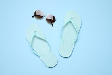 Flip flops and sunglasses on light blue background, flat lay. Beach objects