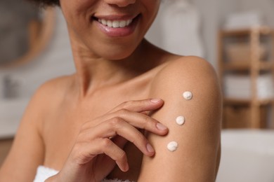 Photo of Young woman applying body cream onto arm in bathroom, closeup