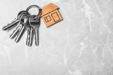 Photo of Keys with trinket in shape of house on grey marble background, top view and space for text. Real estate agent services
