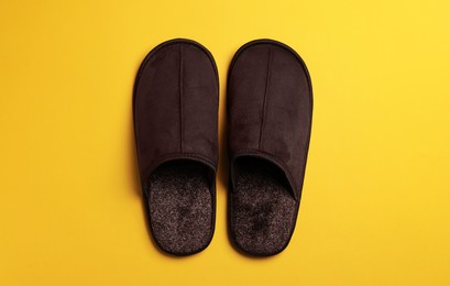 Photo of Pair of brown slippers on yellow background, top view