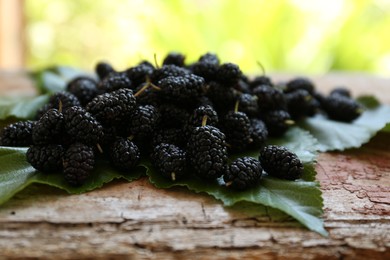 Photo of Heap of delicious ripe black mulberries and green leaves on wooden table against blurred background, closeup