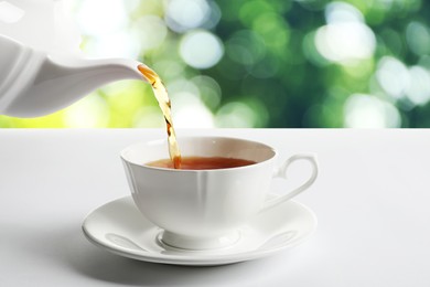 Image of Pouring tea into cup on white table against blurred background