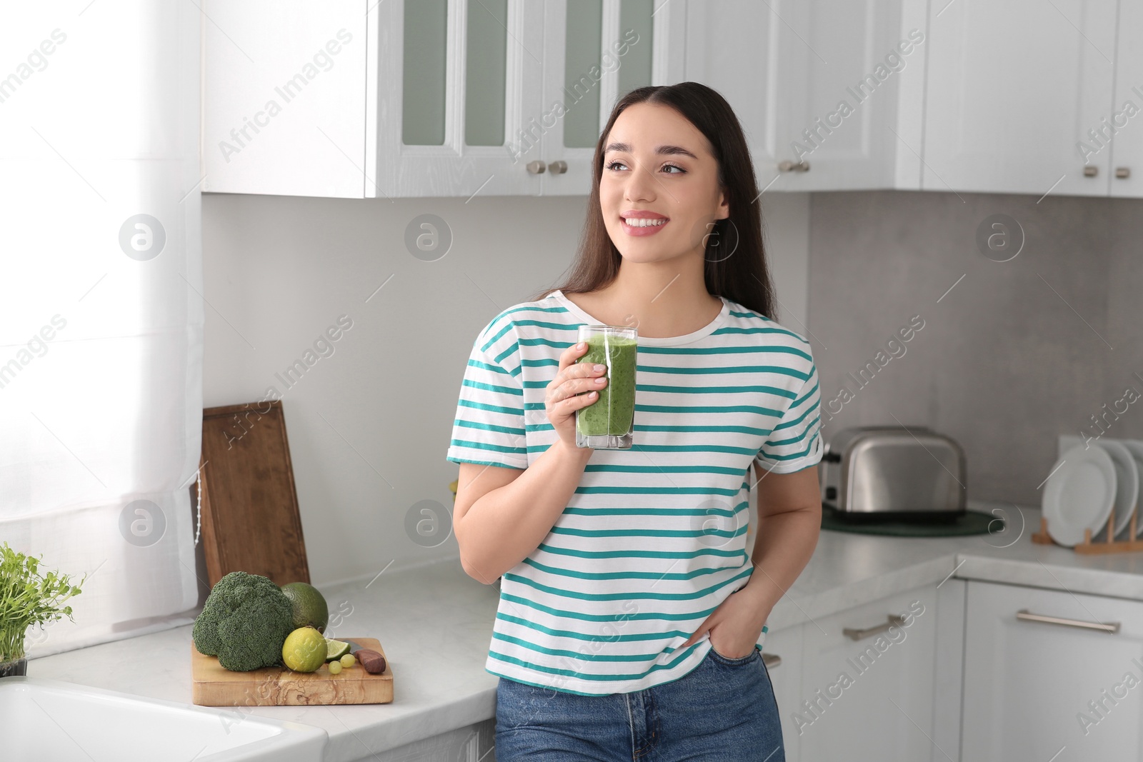 Photo of Beautiful young woman holding glass with tasty smoothie in kitchen