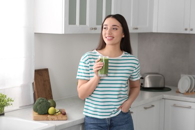 Photo of Beautiful young woman holding glass with tasty smoothie in kitchen