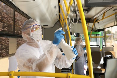 Photo of Public transport sanitation. Workers in protective suits disinfecting bus salon