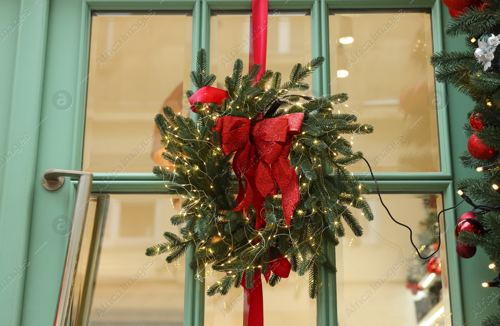 Photo of Beautiful Christmas wreath with ribbon and festive lights hanging on door