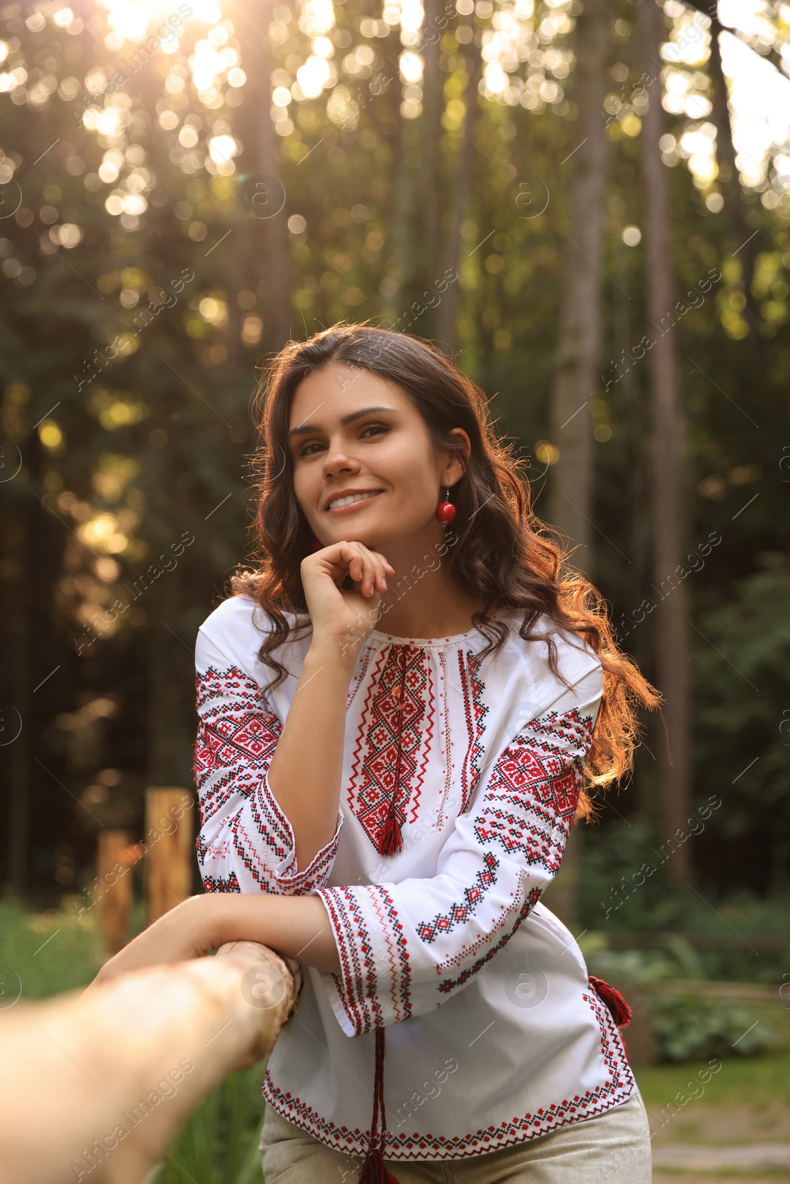 Photo of Beautiful woman wearing embroidered shirt near wooden railing in countryside. Ukrainian national clothes