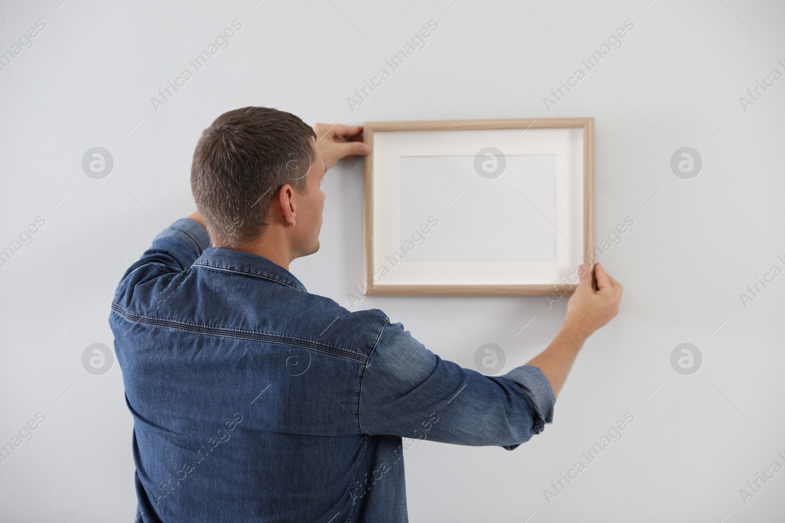 Photo of Man hanging picture on white wall indoors. Interior decoration