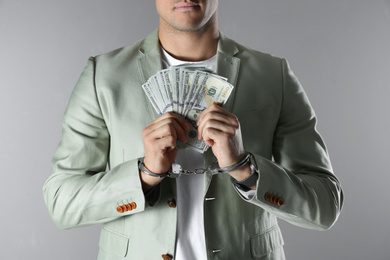 Photo of Man in handcuffs holding bribe money on grey background, closeup