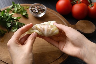 Woman preparing stuffed cabbage roll at table, closeup