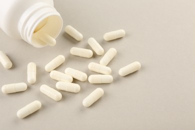 Bottle and vitamin capsules on light background, closeup. Space for text