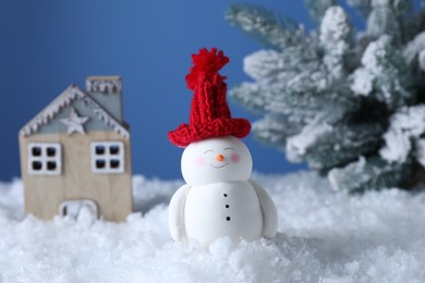 Cute decorative snowman, hut and fir tree on artificial snow against light blue background