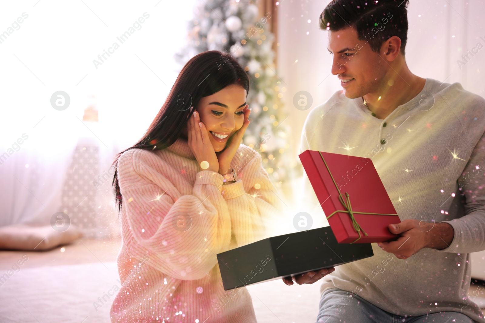 Image of Couple opening Christmas gift with magic light at home