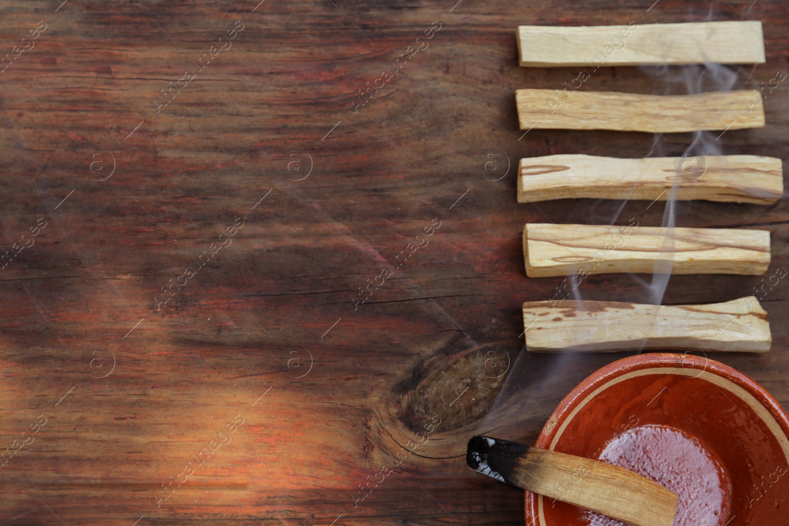 Photo of Palo santo stick smoldering in bowl on wooden table, flat lay. Space for text