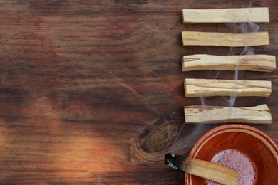 Palo santo stick smoldering in bowl on wooden table, flat lay. Space for text