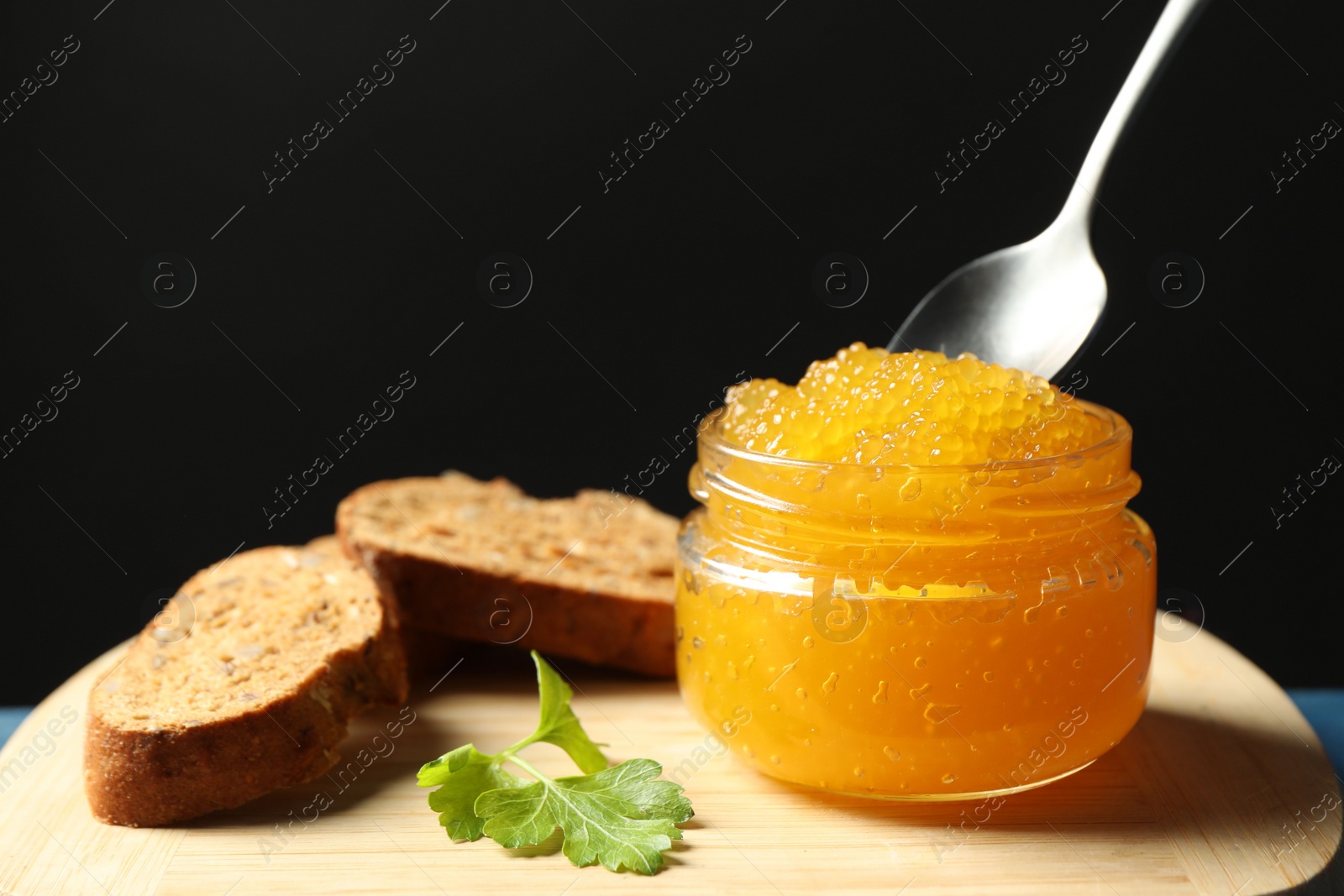 Photo of Fresh pike caviar in glass jar, bread and parsley on wooden board, closeup