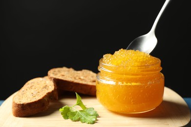 Photo of Fresh pike caviar in glass jar, bread and parsley on wooden board, closeup