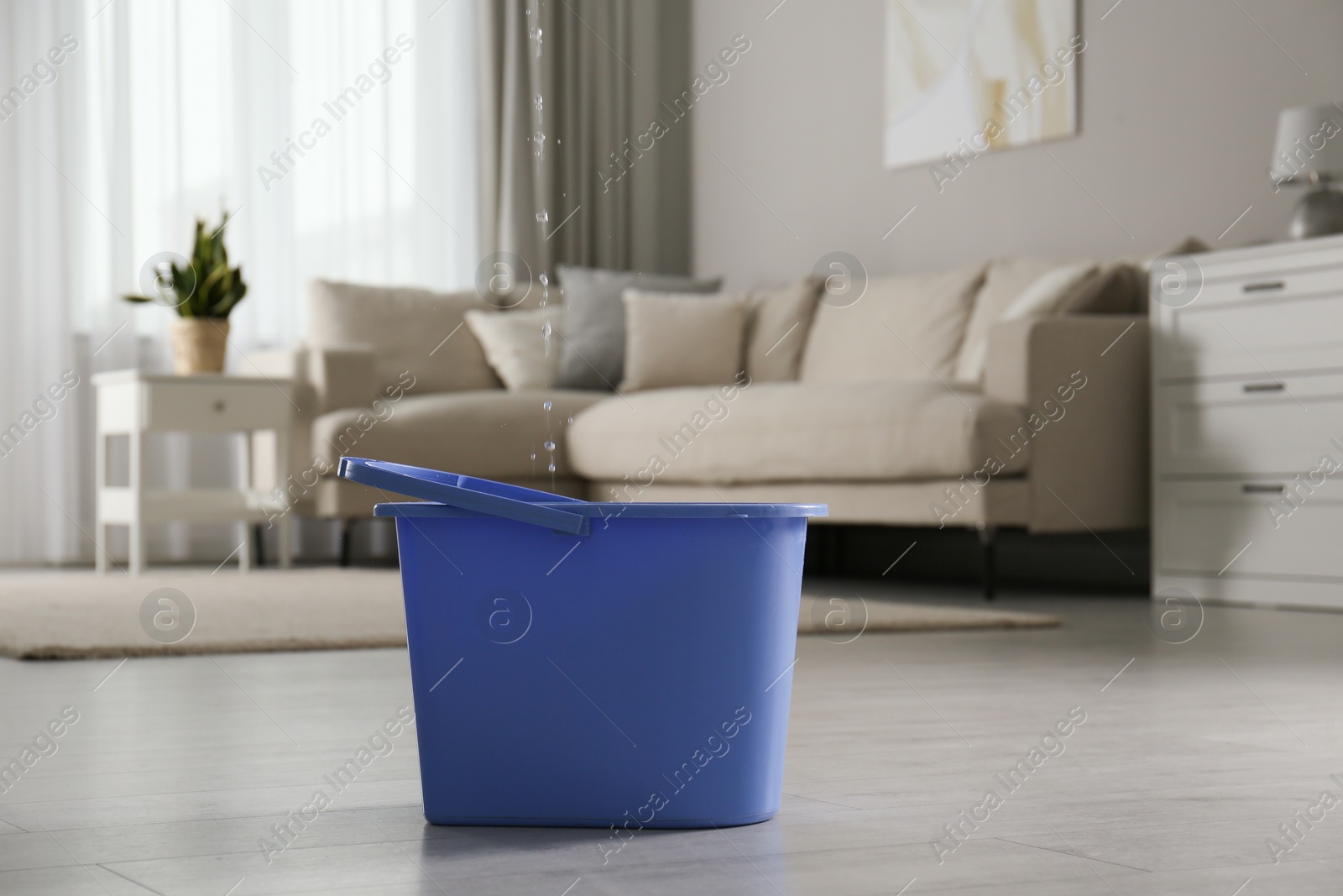 Photo of Water dripping from ceiling into plastic bucket on floor in living room. Leaking roof