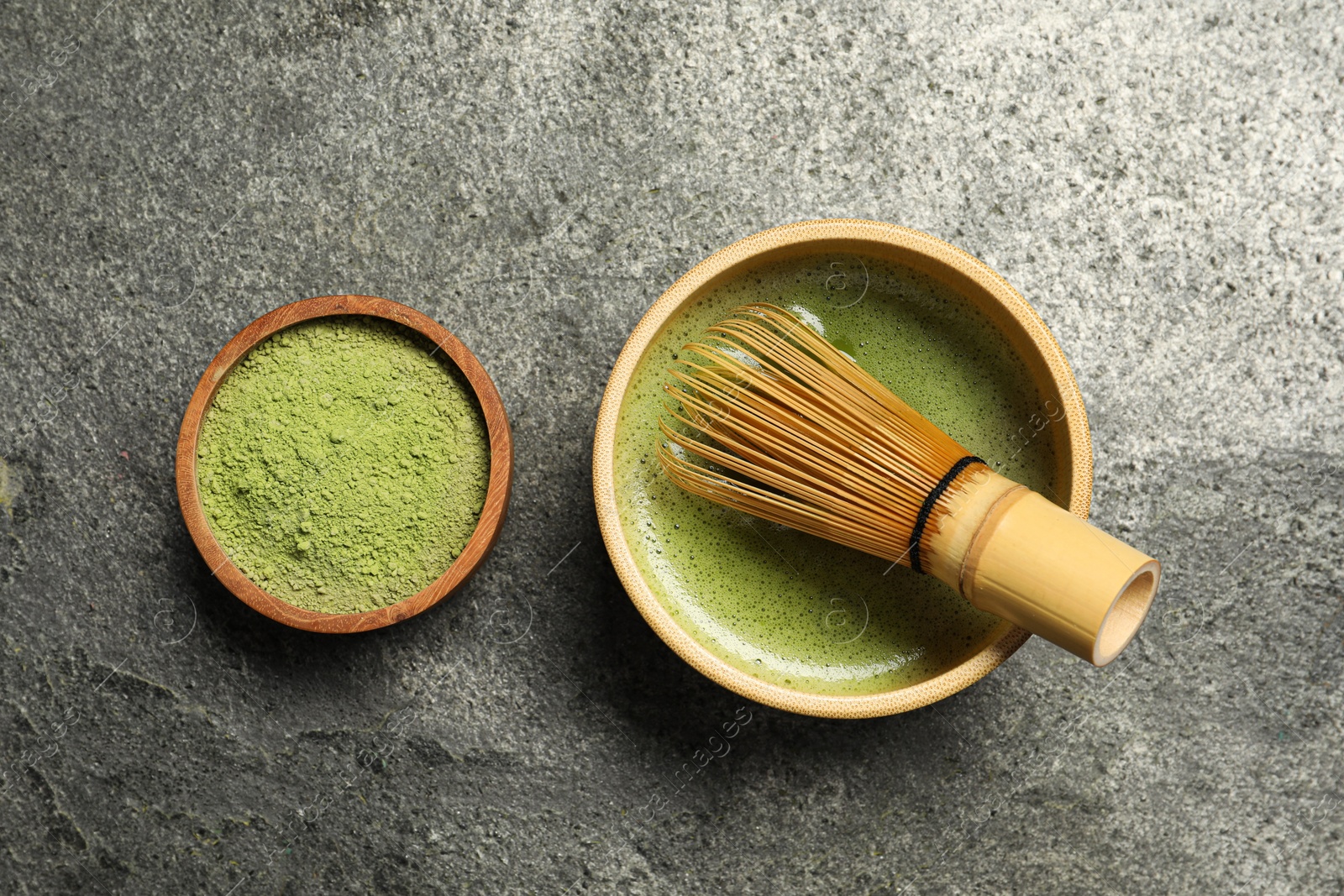 Photo of Cup of fresh matcha tea and green powder on grey table, flat lay