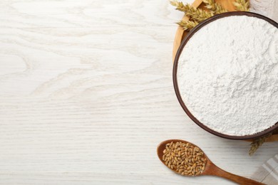 Photo of Organic flour in bowl, spoon with grains of wheat and spikelets on white wooden table, flat lay. Space for text