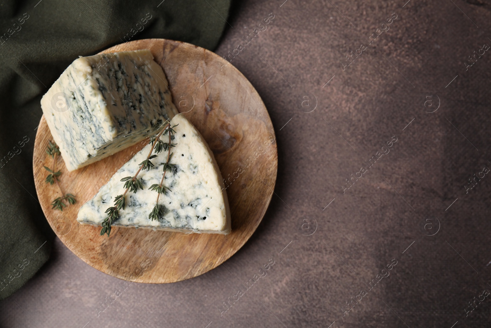 Photo of Tasty blue cheese with thyme on brown table, top view. Space for text