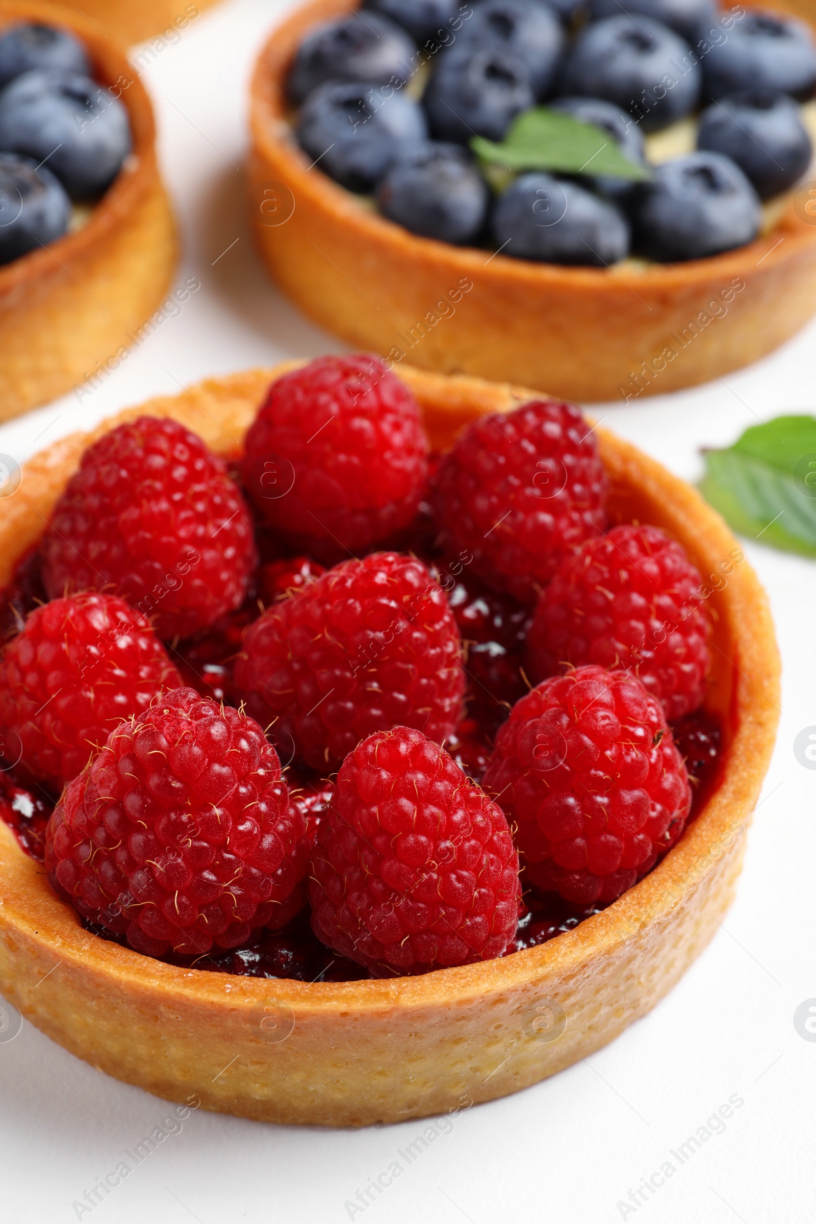 Photo of Tartlet with fresh raspberries on white table, closeup. Delicious dessert