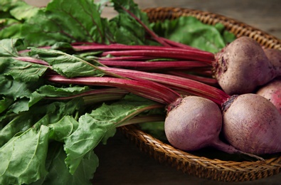 Photo of Wicker basket with bunch of fresh beets on table, closeup