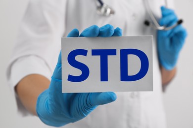 Doctor holding sheet of paper with abbreviation STD on white background, closeup