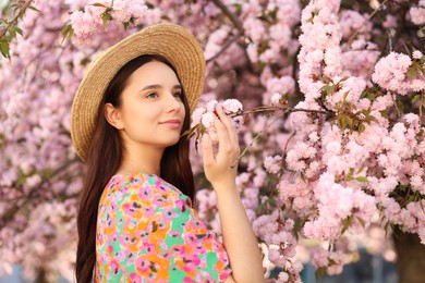 Photo of Beautiful woman in straw hat near blossoming tree on spring day