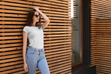 Photo of Young woman wearing gray t-shirt near wooden wall on street. Urban style