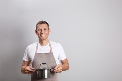 Photo of Happy man with cooking pot on light grey background. Space for text