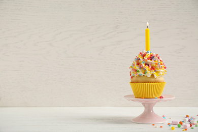Photo of Birthday cupcake with candle on white table against wooden background. Space for text