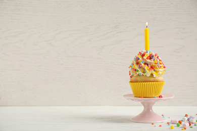 Birthday cupcake with candle on white table against wooden background. Space for text