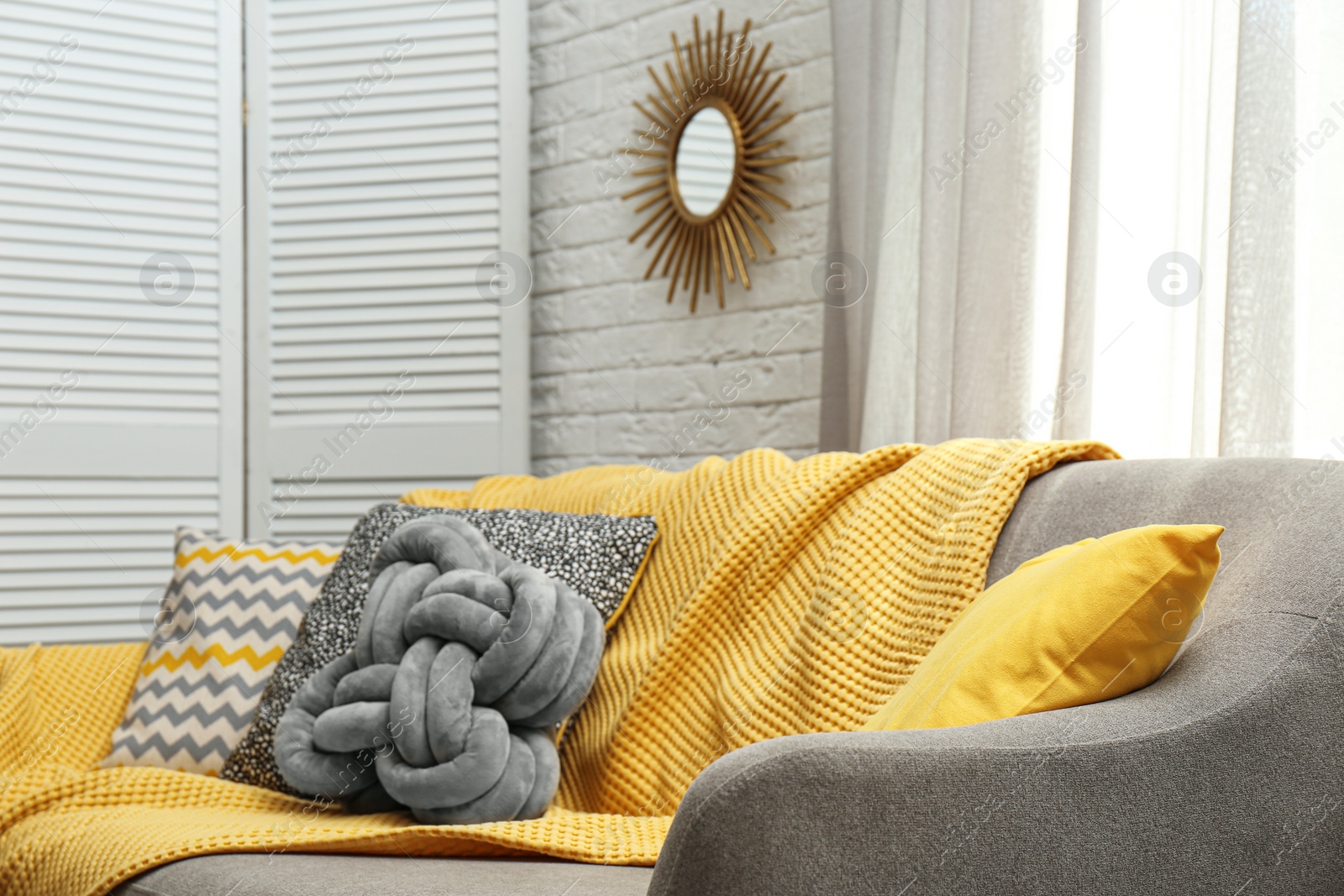 Photo of Soft pillows and yellow plaid on sofa in living room