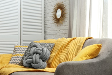 Photo of Soft pillows and yellow plaid on sofa in living room