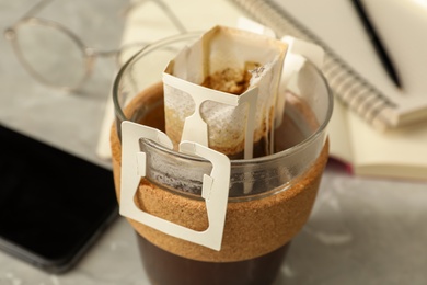 Photo of Glass cup with drip coffee bag on table, closeup