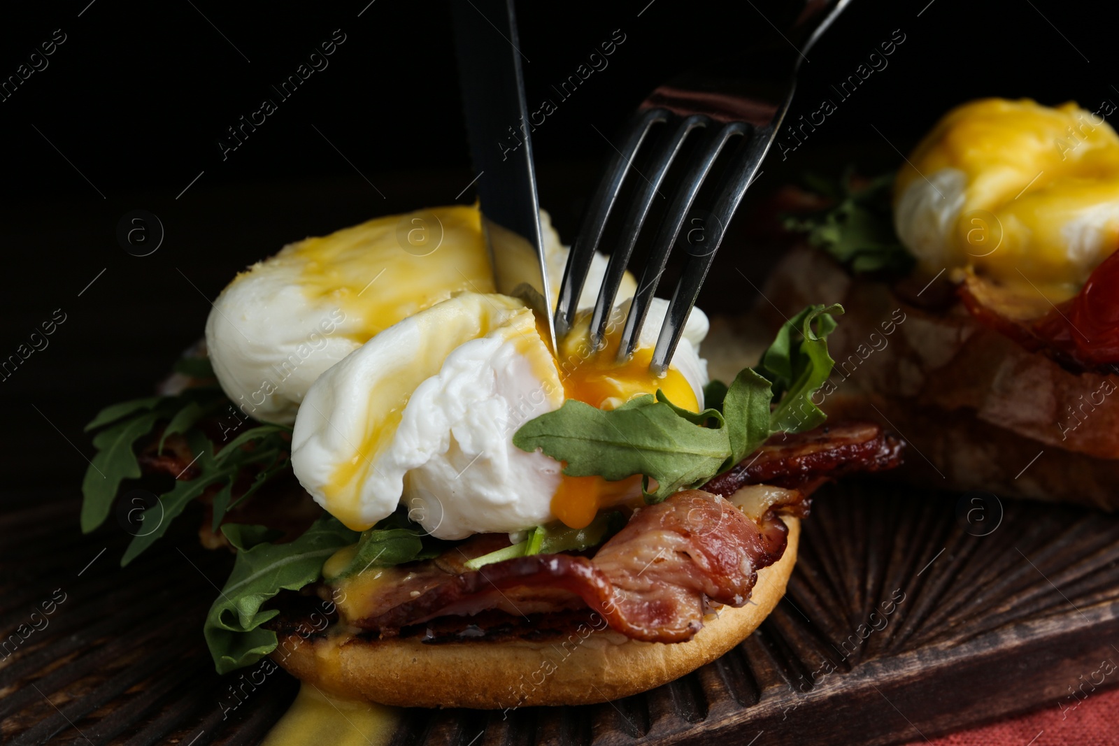Photo of Cutting tasty egg Benedict on wooden board, closeup
