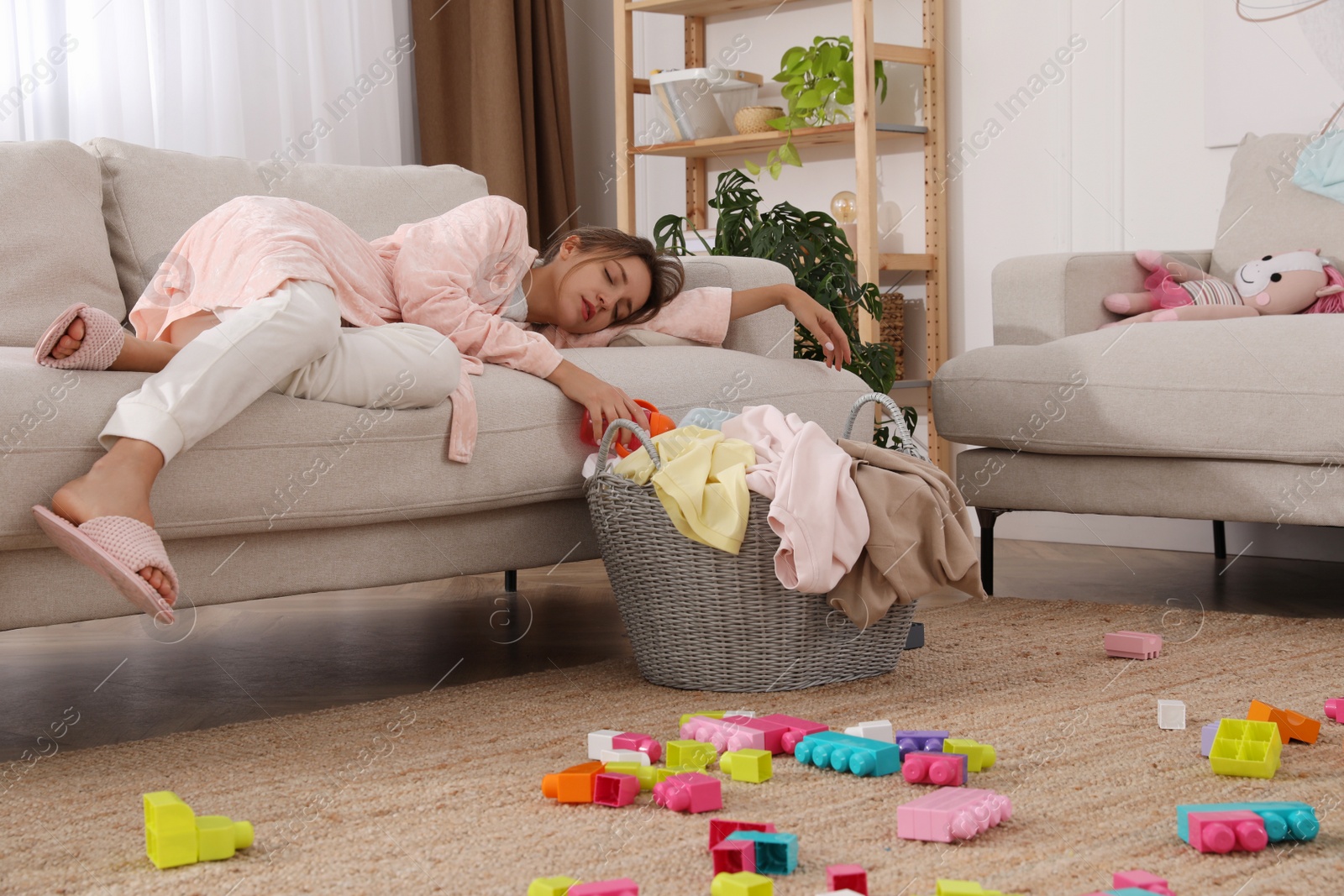 Photo of Tired young mother sleeping on sofa in messy living room