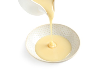 Photo of Pouring condensed milk from jug into bowl on white background. Dairy product