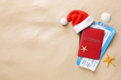 Passport with tickets, Santa hat, seashell, starfish and space for text on sand, flat lay. Christmas vacation