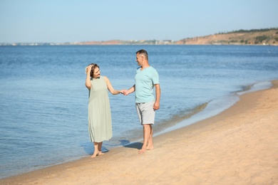 Happy mature couple holding hands at beach on sunny day