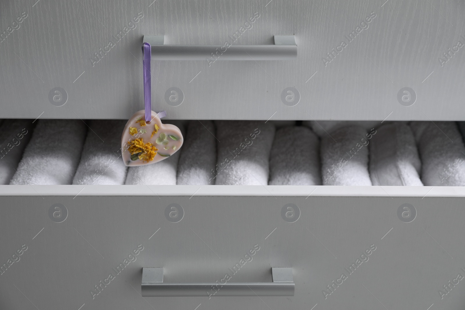 Photo of Chest of drawers with heart shaped scented wax sachet and towels, closeup