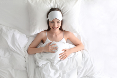 Young woman with sleep mask lying on comfortable pillow in bed at home, top view