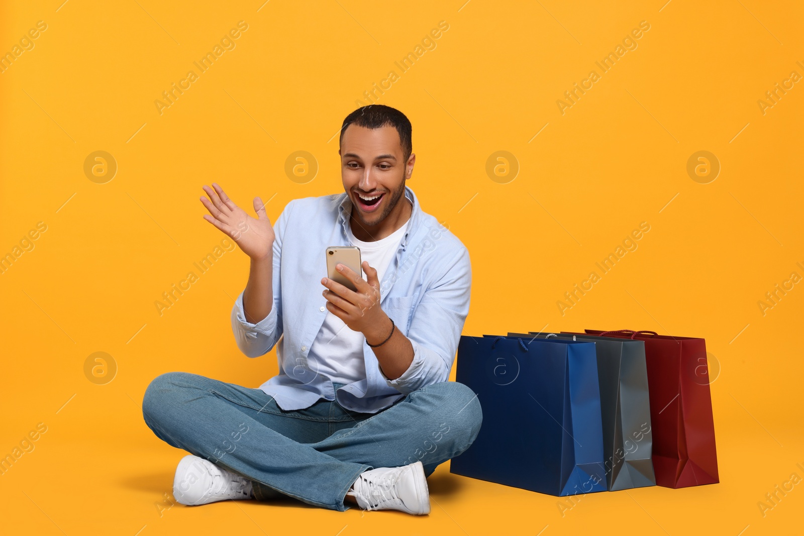 Photo of Happy African American man with shopping bags and smartphone on orange background