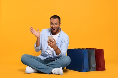 Happy African American man with shopping bags and smartphone on orange background