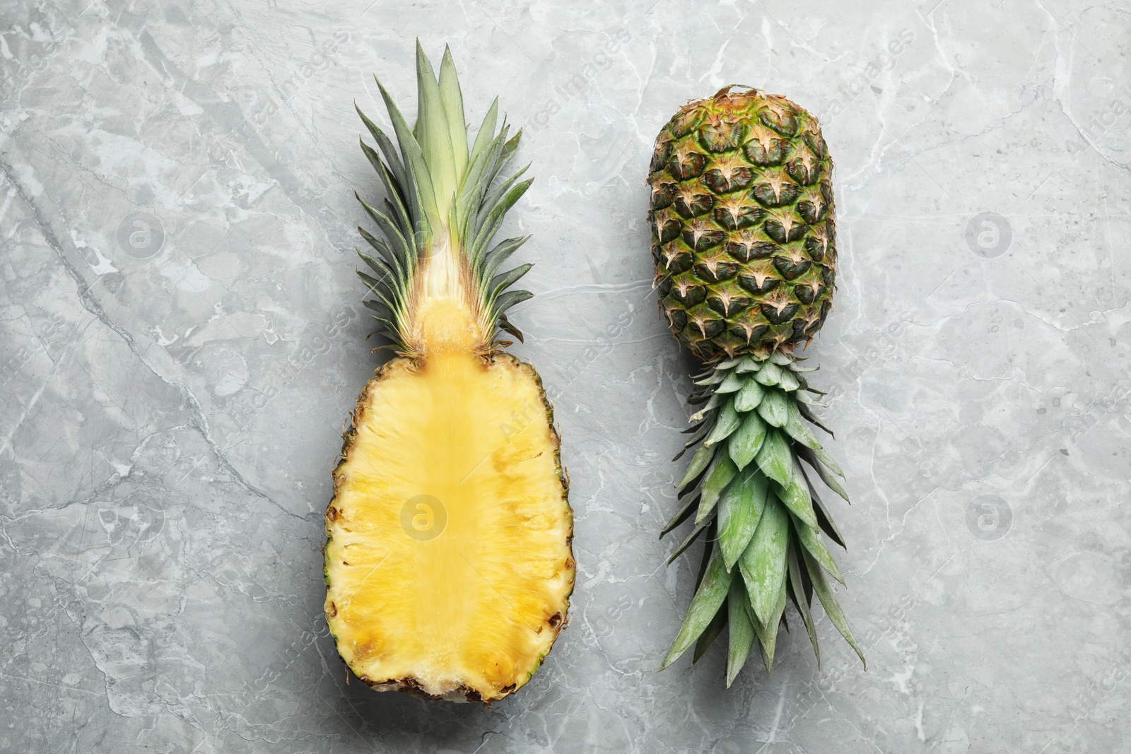 Photo of Fresh whole and cut pineapples on gray marble background, top view