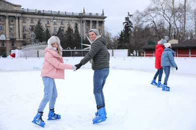 Image of Happy couple skating along ice rink outdoors