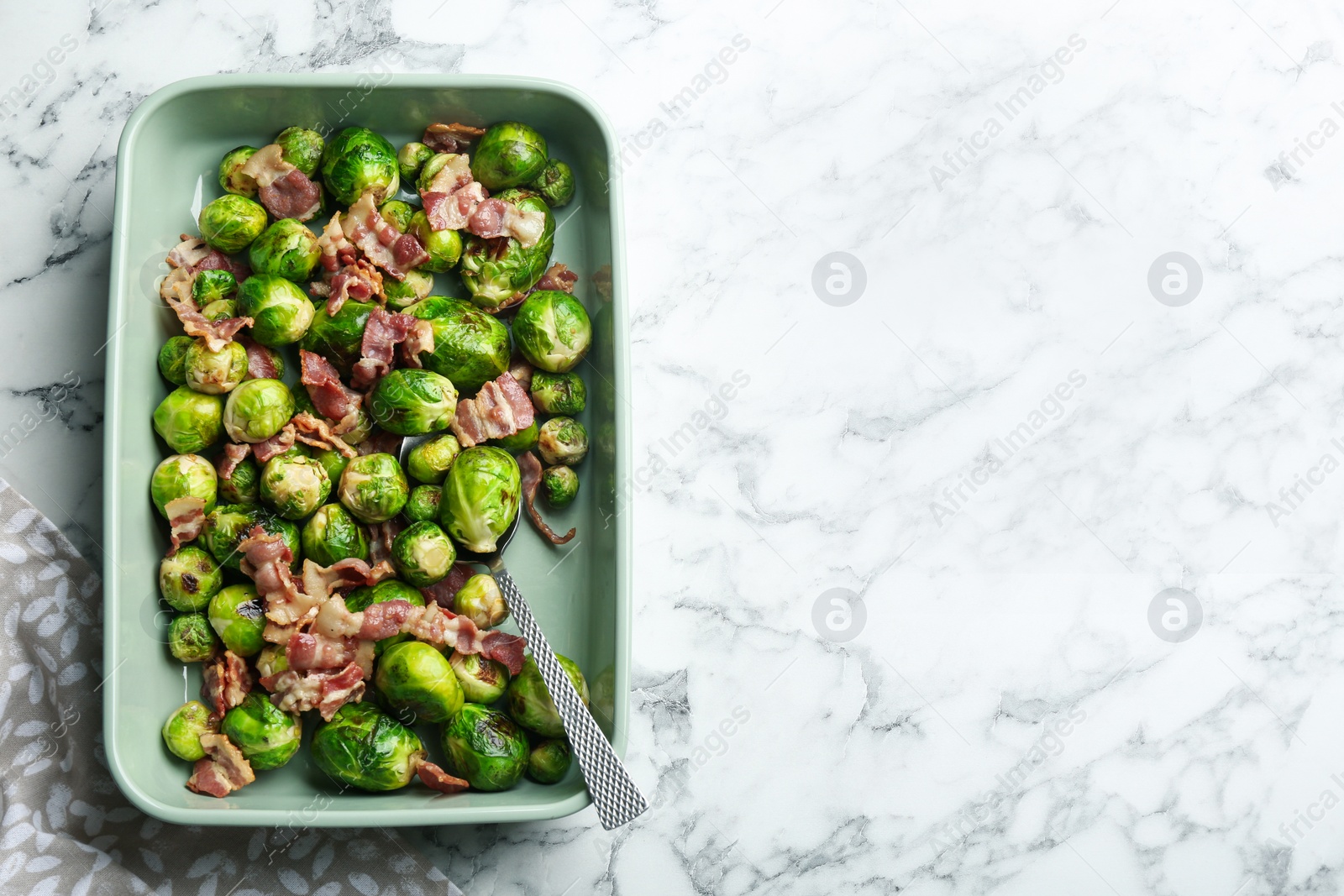 Photo of Delicious Brussels sprouts with bacon on white marble table, top view. Space for text