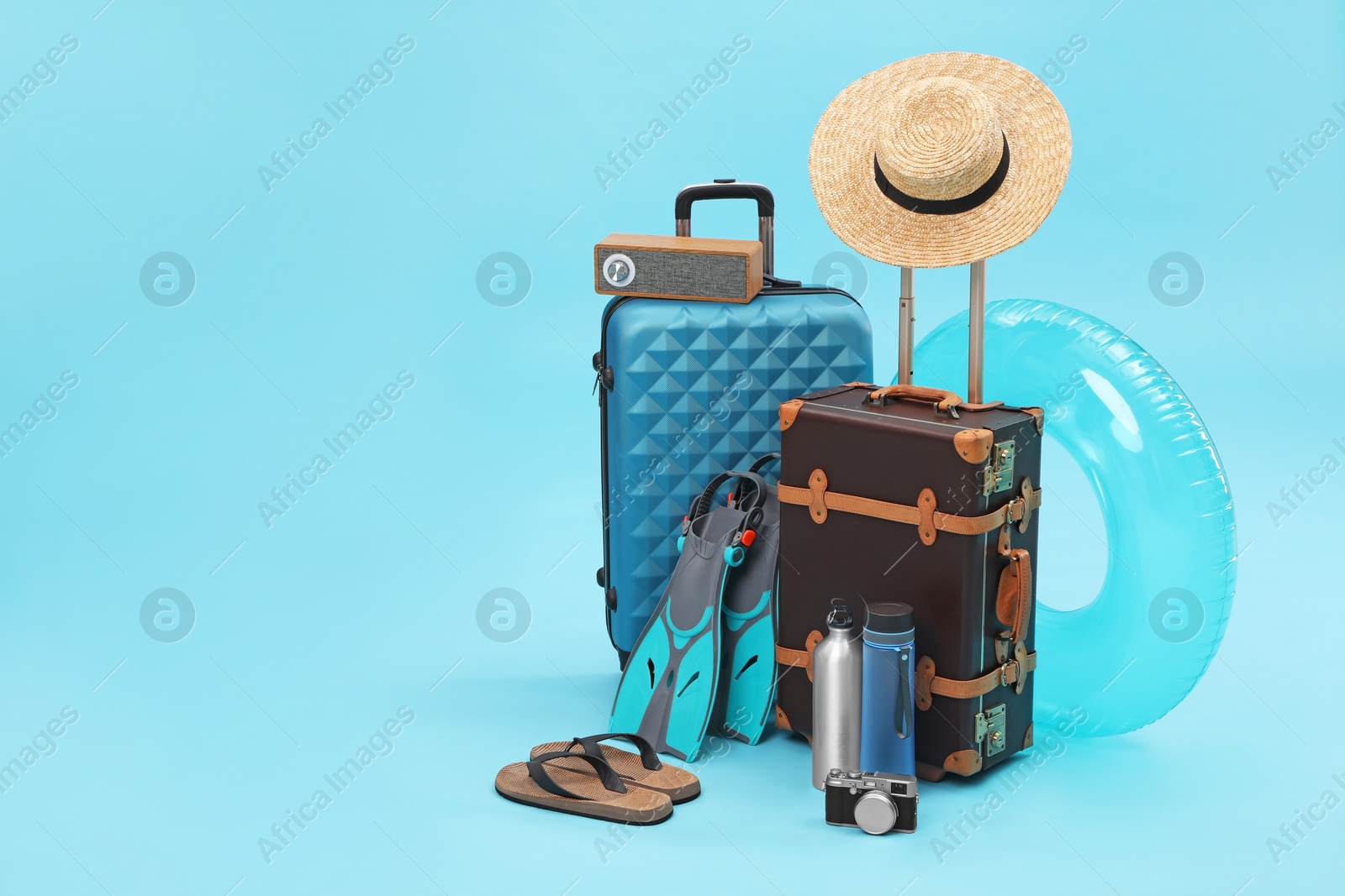 Photo of Suitcases, portable bluetooth speaker and beach accessories on light blue background, space for text. Summer vacation